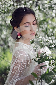 portrait of a young beautiful woman in white clothes standing next to a blooming cherry tree in spring.