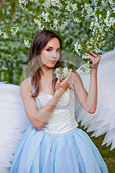 Portrait of a young beautiful woman in a white corset and with large white angel wings behind her back