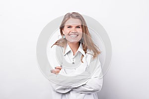 Portrait of young beautiful woman in white shirt smiling and standing with crossed arms over white background