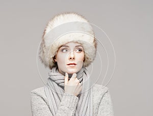 Portrait of a young and beautiful woman in a winter hat over grey background.