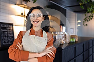 Portrait of young beautiful woman worker in cafe restaurant, Hispanic woman with curly hair and glasses smiling and