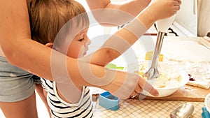 Portrait of young beautiful woman teaching her little child boy making cookies and baking pies on kitchen at home