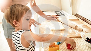 Portrait of young beautiful woman teaching her little child boy making cookies and baking pies on kitchen at home