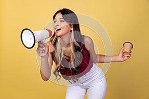 Portrait of young beuatiful girl, student in casual style clothes shouting at megaphone isolated on yellow studio