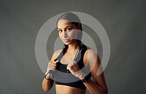Portrait of young biracial woman in sports bra holding jump rope over shoulders in studio