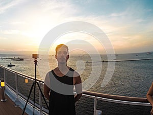 Portrait of a young black male tourist on the deck of a cruise ship in front of a sunset sky. African tourist on the beach trip