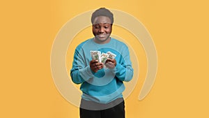 Portrait of young black man counting dollar banknotes and smiling, studio with orange background