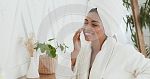 Portrait of young black woman in bathrobe and towel on head applying cream on face and smiling, slow motion