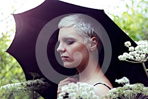 Portrait of a young blond girl with an umbrella in the meadow