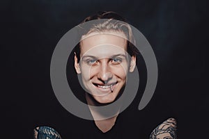 Portrait of a young blond guy with tattoos and piercings on a black background photo