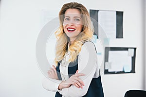 Portrait of young blond smiling businesswoman wearing smart suit stands in her bright office, work concept