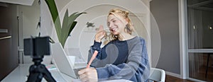 Portrait of young blond smiling woman, studying at home, remote education concept, connects to online course or lesson