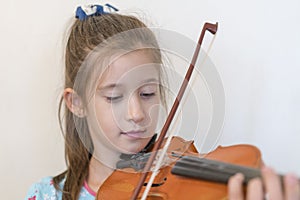 Portrait of a young blond teenage girl playing violin. Girl playing the violin on a light background.