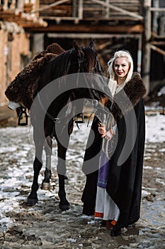 Portrait of a young blond woman in a black cloak with a horse.
