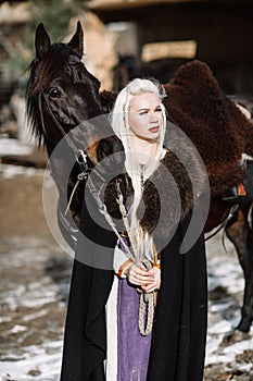 Portrait of a young blond woman in a black cloak with a horse.