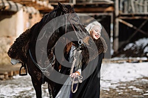 Portrait of a young blond woman in a black cloak with a horse.