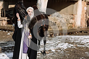 Portrait of a young blond woman in a black cloak with a horse.