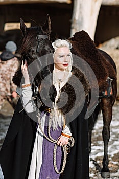 Portrait of a young blond woman in a black cloak with a horse.