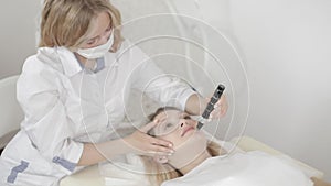 Portrait of young blond woman doctor cosmetologist dermatologist using dermatoscope for skin examination of face or