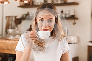 Portrait of young blond woman drinking coffee while sitting in cozy cafe indoor