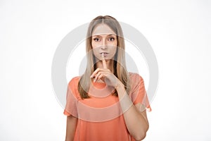 Portrait of young blond woman keeping finger at her mouth, saying Shh, Hush, Tsss. Silence and secret concept