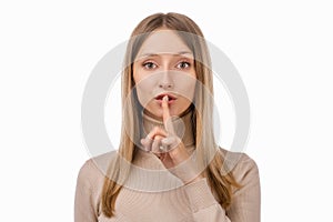 Portrait of young blond woman keeping finger at her mouth, saying Shh, Hush, Tsss. Silence and secret concept