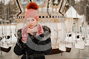 Portrait of young blond woman in winter clothes. Red cap and mittens. Walking in the park