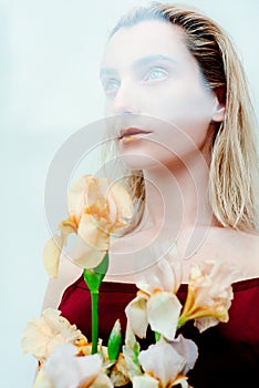 Portrait of the young blonde attractive woman with the fashion alien gold make up standing with the iris flowers