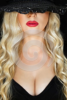 Portrait of a young blonde in a black hat with a decollete, over a black background. Close-up. photo