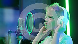 Portrait of young blonde boy singer in headphones singing song in music recording studio. Caucasian kid records new