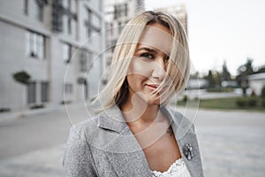 Portrait of young blonde businesswoman in gray suit walking in the city