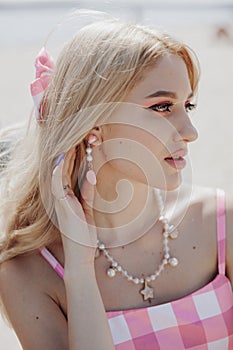 Portrait of young blonde girl looking like a Barbie doll in pink dress, ping bow in her head and jewelry