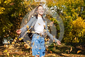 Portrait of a young blonde girl in stylish ripped jeans posing in an autumn park