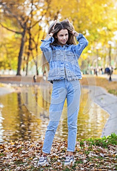 Portrait of a young blonde girl in stylish ripped jeans posing in an autumn park