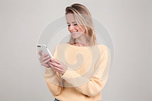 Portrait of young blonde smiling woman using cell phone, messaging, being happy to chat with her boyfriend. wearing yellow sweater