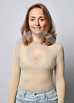 Portrait of young blonde woman in beige shirt, bodysuit with long sleeves and jeans with open friendly smile