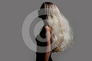 Portrait of a young blonde woman with lush wavy hair. face in shadow. Gray background