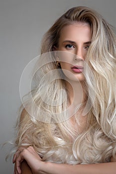 Portrait of a young blonde woman with lush wavy hair. Gray background