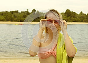 Portrait of a young blonde woman in red glasses with a towel near the river. Girl resting