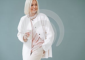 Portrait of young blonde woman in sportswear with thermocup on background of grey wall