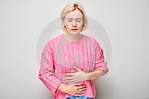 Portrait of young blonde woman suffering from stomach pain isolated on white studio background. Intestinal and stomach problems