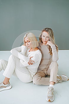 Portrait of young blonde women friends in sportswear on background of grey wall