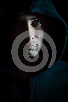 Portrait of a young blue-eyed man with a hood covering his head who in the shadow has a serious and determined look