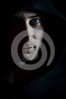 Portrait of a young blue-eyed man with a hood covering his head who in the shadow has a serious and determined look