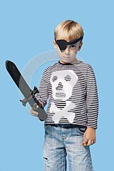 Portrait of a young boy in pirate costume holding sword over blue background
