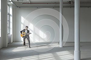 Portrait of a young boy playing the guitar. He is wearing a black suit