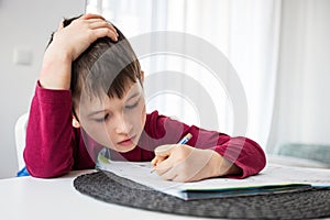 Portrait of young boy struggling with his homework at home. Children home education concept. Distance learning