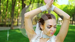 Portrait of young bride with makeup and crystals on face dancing in sunlit park