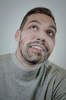 Portrait of a young brown-haired man with a short beard and a gray turtleneck sweater that is looking up