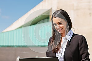 Portrait of a young brunette businesswoman working on laptop outside the office